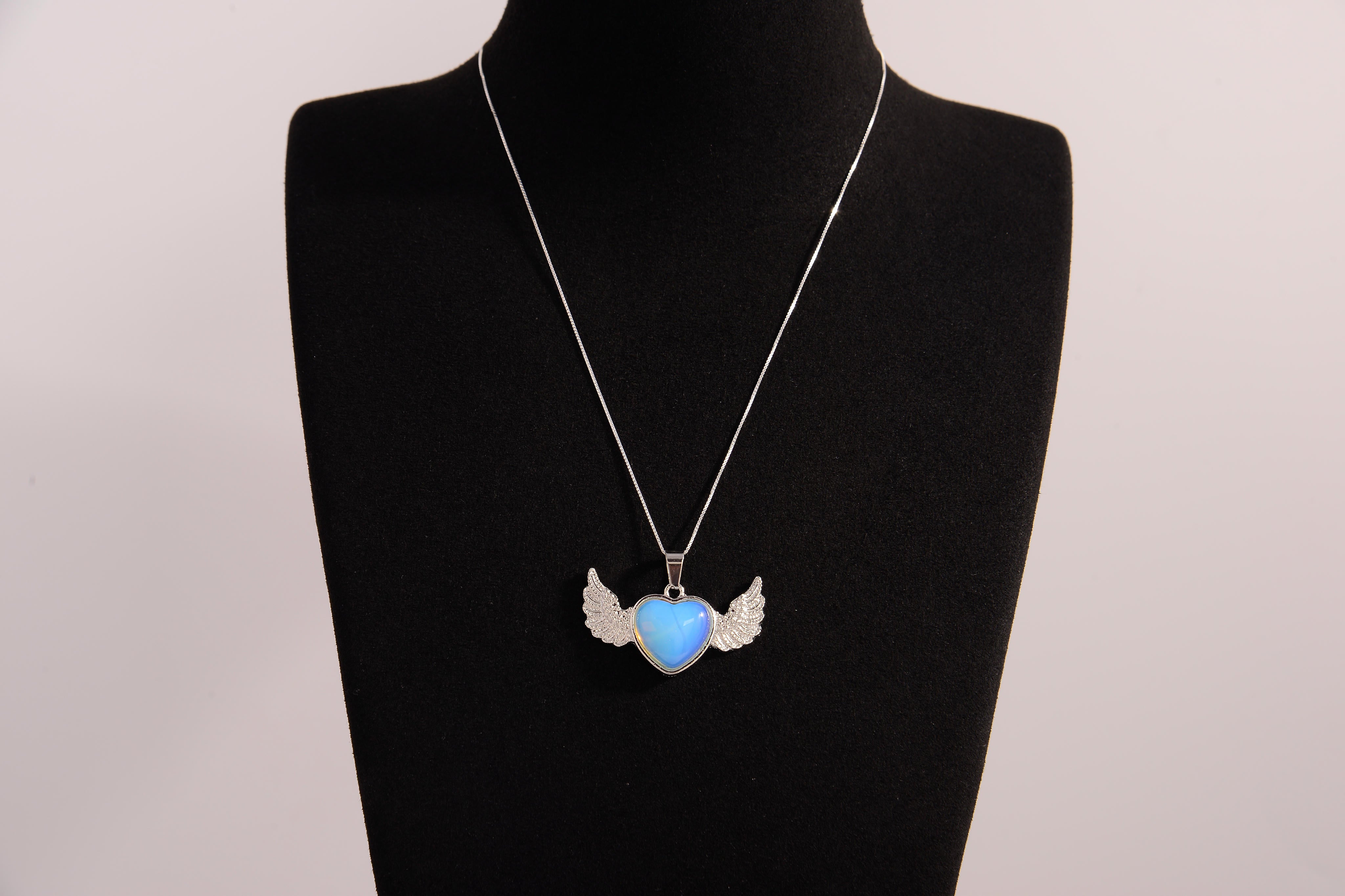Raw Earth Crystals opalite heart with wings necklace, featuring a luminous blue heart-shaped stone adorned with delicate angelic wings, designed to enhance emotional healing, promote inner peace, and inspire spiritual connection.