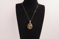 Raw Earth Crystals tiger eye pendant with a teardrop-shaped design, featuring natural tiger eye and an ornate silver-tone setting, promoting confidence, focus, and protection.
