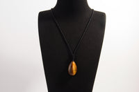 Raw Earth Crystals tiger eye teardrop pendant on black cord, crafted from natural tiger eye stone, promoting confidence, focus, and personal power.